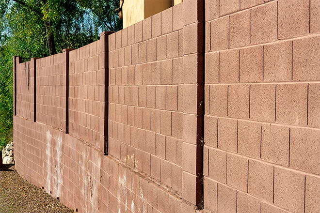 Red brick retaining wall in late afternoon sunlight with gravel floor and trees in background