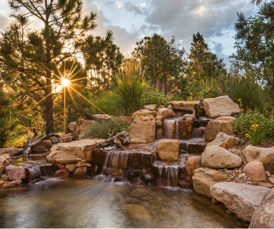 the sun shines through the clouds over a small waterfall.