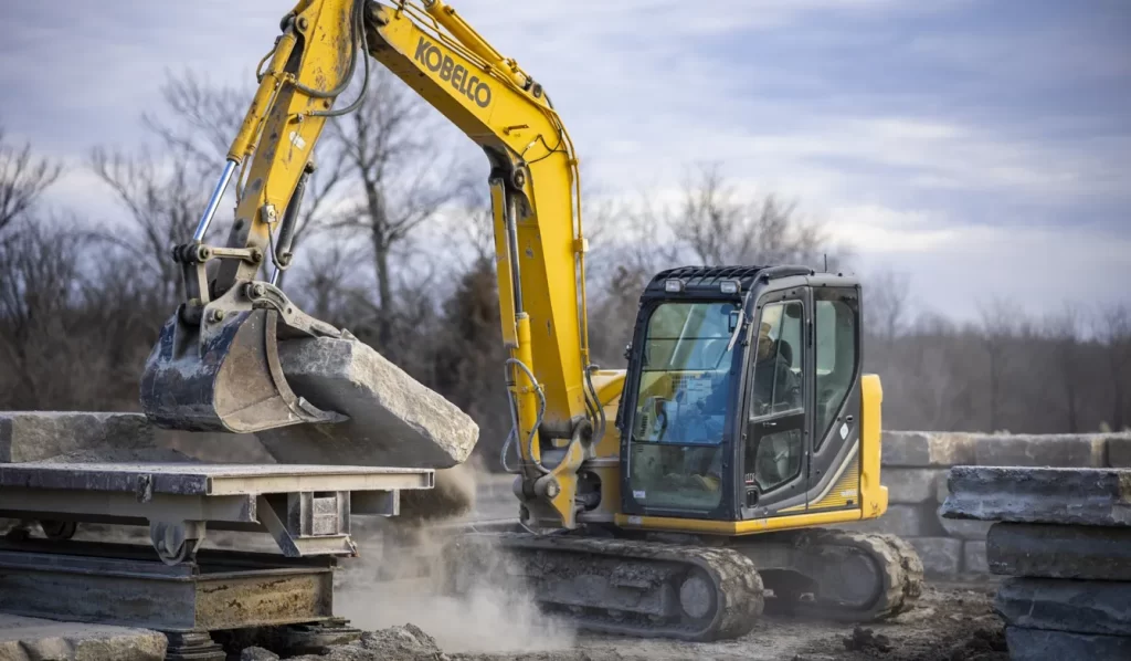 Excavator lifting large stone on construction site.